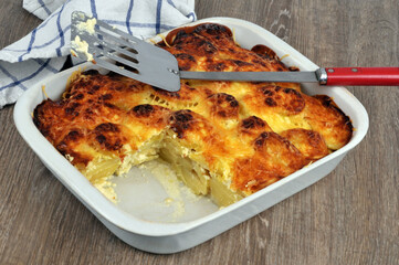 Plat de gratin de pommes de terre entamé avec une spatule de cuisine