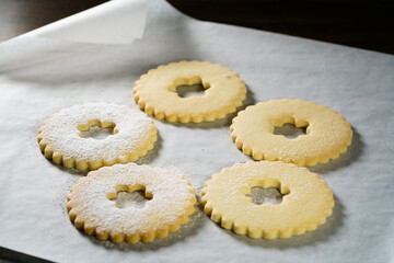 Making Linzer cookies, sprinkling tops with powdered sugar. White parchment paper, dark background, high resolution