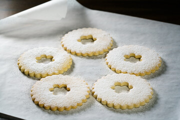 Tops of Linzer cookies covered in powdered sugar. White parchment paper, dark background, high resolution