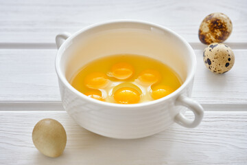 Fresh and useful quail eggs in a white cup on a white wooden table close-up