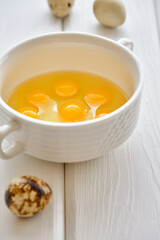 Fresh and useful quail eggs in a white cup on a white wooden table close-up