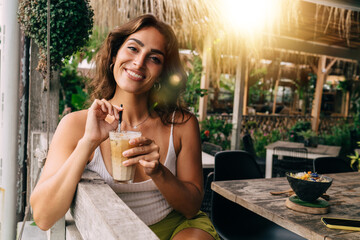 Delighted woman drinking ice coffee in outdoor summer cafe