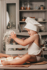 charismatic girl in an apron and a hat is sitting and rolling out the dough