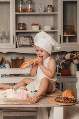 charismatic girl in an apron and a hat is sitting and rolling out the dough