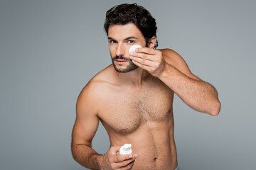 shirtless man applying toner on face with cotton pad isolated on grey