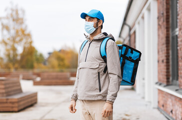 food shipping, pandemic and people concept - delivery man in protective medical mask with thermal insulated bag in city