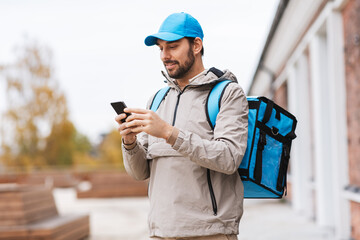 food shipping, profession and people concept - happy smiling delivery man with smartphone and thermal insulated bag in city