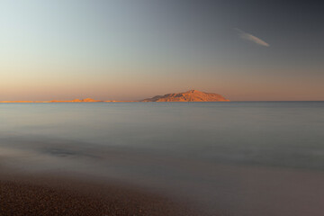 Seascape, across the smooth surface of the water, the desert cliffs are illuminated by the sunset