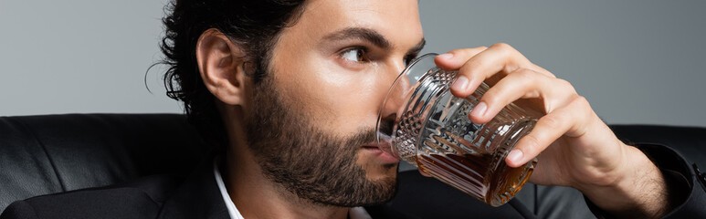 bearded man with wavy hair drinking whiskey isolated on grey, banner