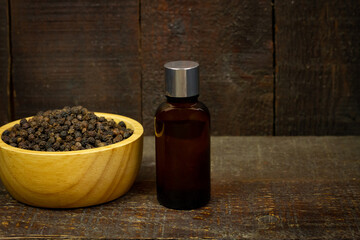 Black pepper essential oil in glass bottle with peppercorn on wooden bowl on rustic wooden background.