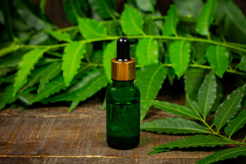 Neem oil in bottle and neem leaf with branch on wooden background.