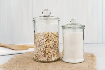 Two pantry jars with oats and white sugar, glass jars mockup for food sticker or label presentation. - obrazy, fototapety, plakaty