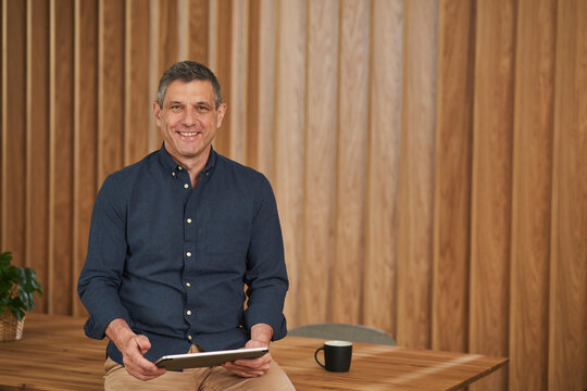 Businessman smiling while sitting with tablet on conference table in board room