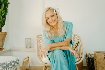 Senior woman with flower in long white hair sitting on chair at home