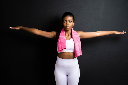 Young woman exercising with arms outstretched against black background