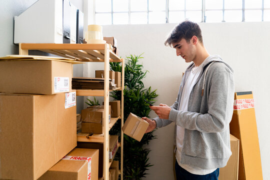 Male entrepreneur scanning QR code through smart phone in front of rack at warehouse