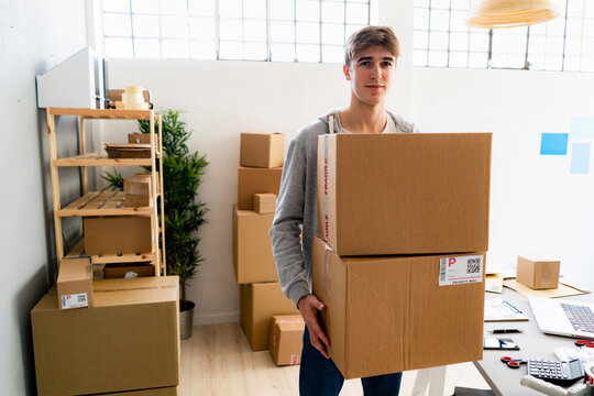 Male entrepreneur carrying cardboard boxes in warehouse