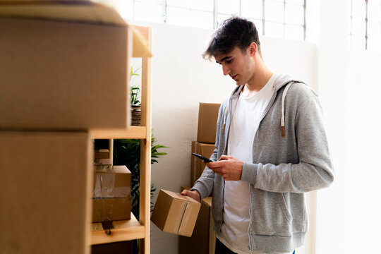 Businessman scanning bar code on box while standing in front of rack at warehouse