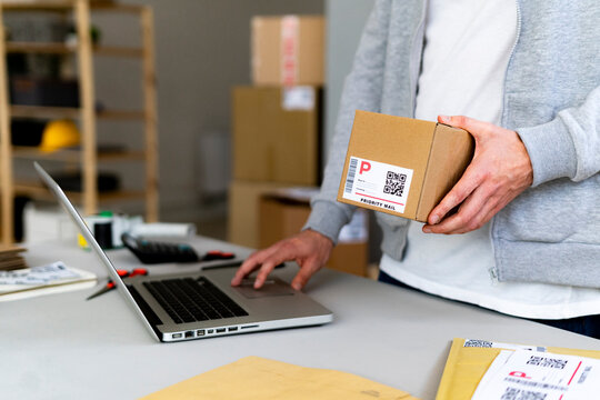 Young businessman holding cardboard box while using laptop at desk