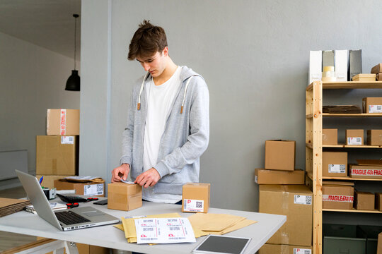 Young businessman sticking bar code label on package at desk in office