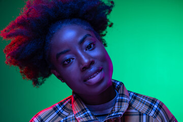 Close-up African young girl's portrait on dark green studio background in purple neon light. Afro hairdo. Concept of human emotions