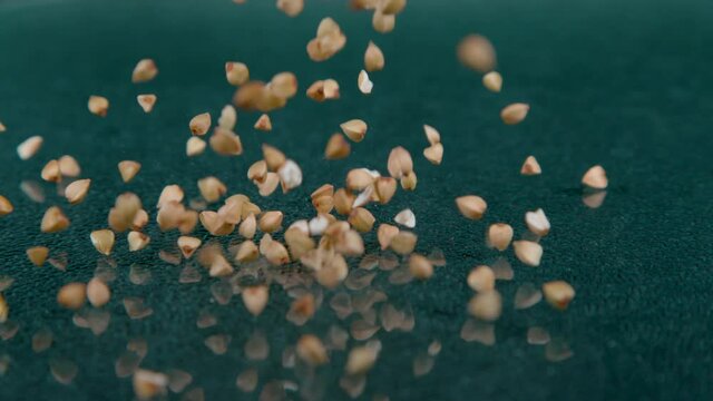 SLOW MOTION, MACRO, DOF: Tiny seeds of buckwheat falls onto the polished surface of an empty countertop. Cinematic shot of organically grown brown groats bouncing across the polished kitchen table.