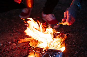 Man roasting meat over wood burning stove while camping at night