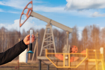 A hand holds a test tube with crude oil on the background of an oil rocking chair