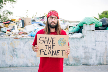 Hippie man with bandana holding save the planet cardboard near garbage dump