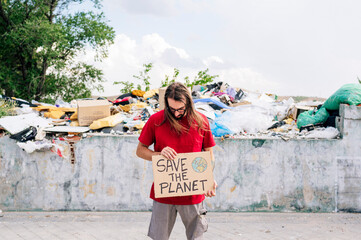 Man holding save the planet cardboard in front of garbage dump