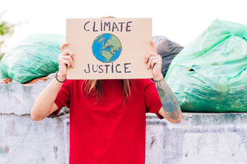 Man covering face with climate justice cardboard near garbage dump