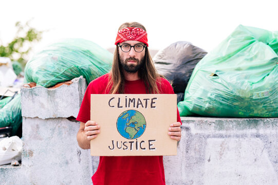 Hippie man holding climate justice cardboard near garbage dump
