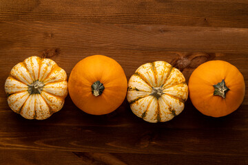 Four pumpkins lie in a row in the middle on a brown wooden background, top view