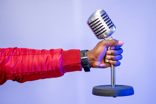 Male influencer's hand holding microphone over purple wall at studio