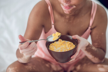 Obraz na płótnie Canvas A dark-skinned woman eating cereals while sitting on bed
