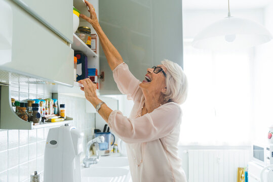 Cheerful senior woman doing chores in kitchen at home