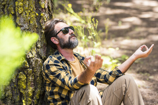Mature man meditating while leaning on tree trunk in forest