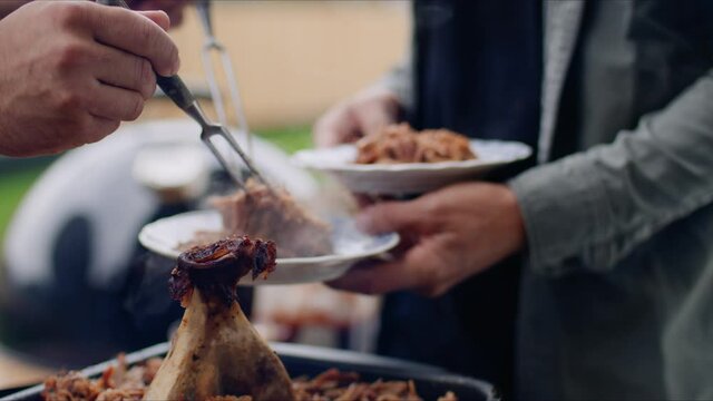 Putting pulled pork on two plates held by a man with two forks in garden