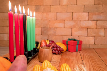 Kwanzaa holiday concept with decorate seven candles red, black and green, gift box, pumpkin,corn and fruit on wooden desk and background.