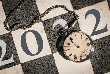 Countdown to 2022 with a vintage pocket watch over a marble chessboard. 