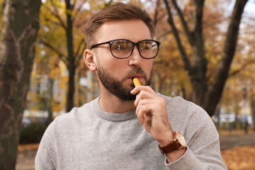 Handsome young man using disposable electronic cigarette in park on autumn day