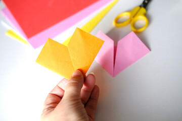 close-up of female hands fold colored paper, makes hearts using origami technique for valentine's...