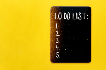 Black digital tablet with to do list on yellow background with blurred lights bokeh