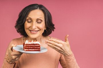 Happy smiling mature aged senior woman holding a birthday cake isolated over pink background.