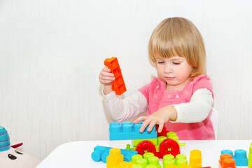 Cute funny little toddler girl playing with building toy blocks building a tower on the table. Kids are playing. Child and toys. Close-up. Copy space.