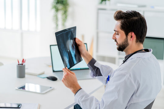 Male healthcare worker analyzing X-ray while sitting at desk in hospital