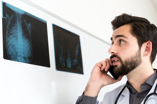 Male doctor looking at X-ray while talking on mobile phone