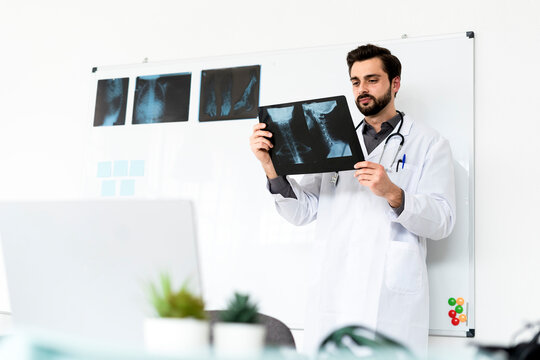 Male healthcare worker analyzing X-ray while standing in front of white board in hospital
