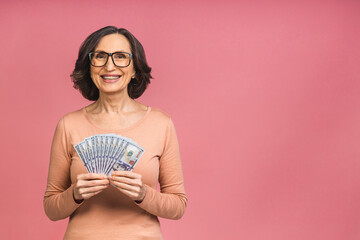 Happy winner! Image of a mature senior happy old woman standing isolated over pink background, holding money. - 473815842