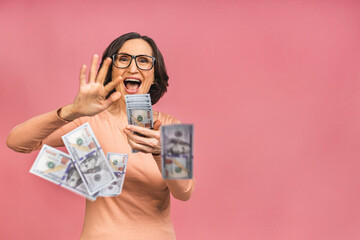Happy winner! Image of a mature senior happy old woman standing isolated over pink background, holding money. - 473816068